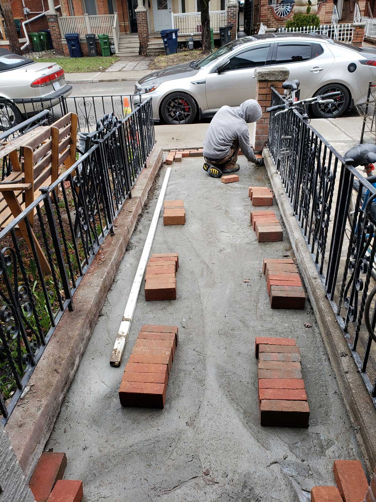 groups of bricks laid across foundation of pathway in front of house lined by black metal fence