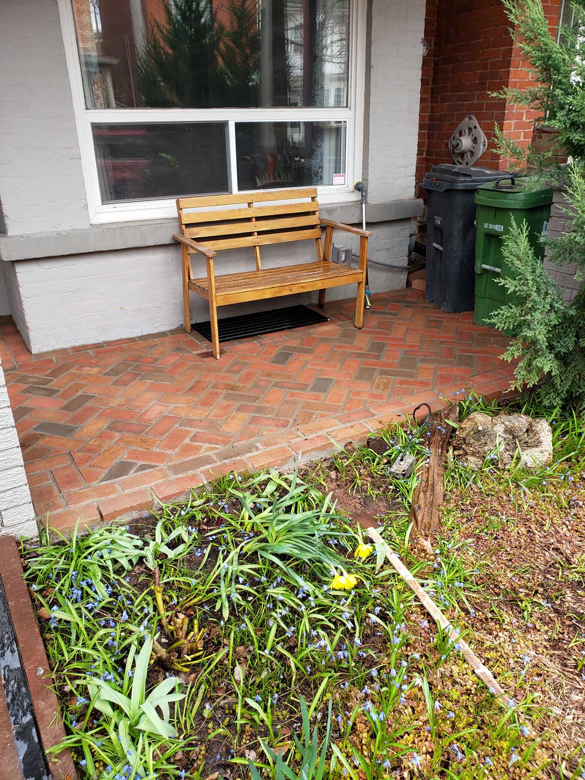 front home porch with patterned brick floor and wooden bench on top in front of window