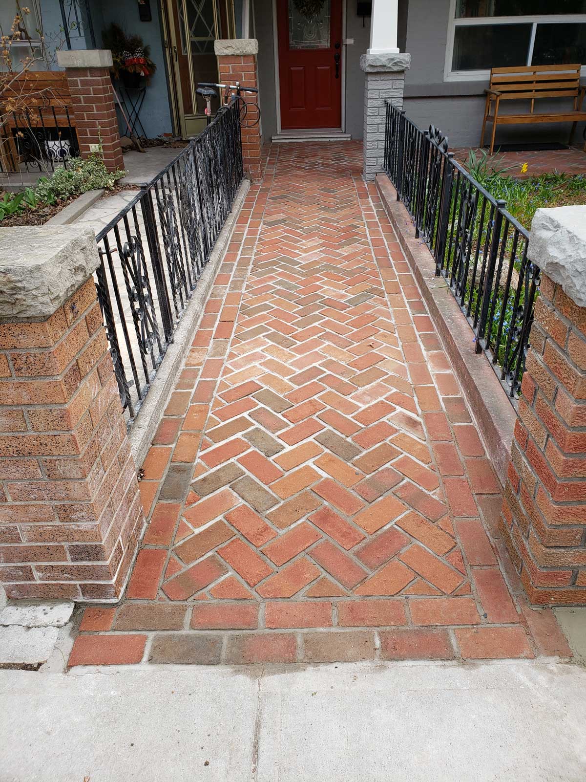 patterned brick pathway in front of home lined by low black fences